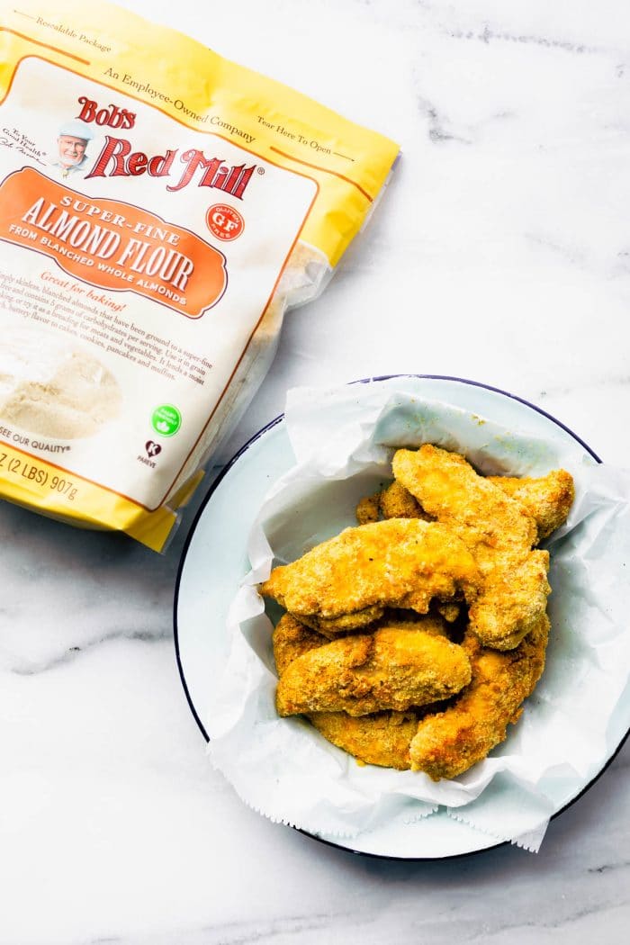 bag of Bob's Red Mill brand almond flour next to white serving bowl filled with air fryer chicken tenders.