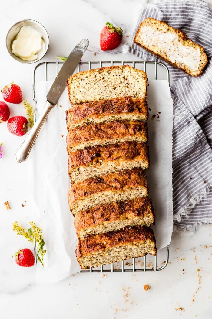 Cinnamon Almond Flour Bread cut into thick slices on parchment-lined cooling rack with butter knife on the side.