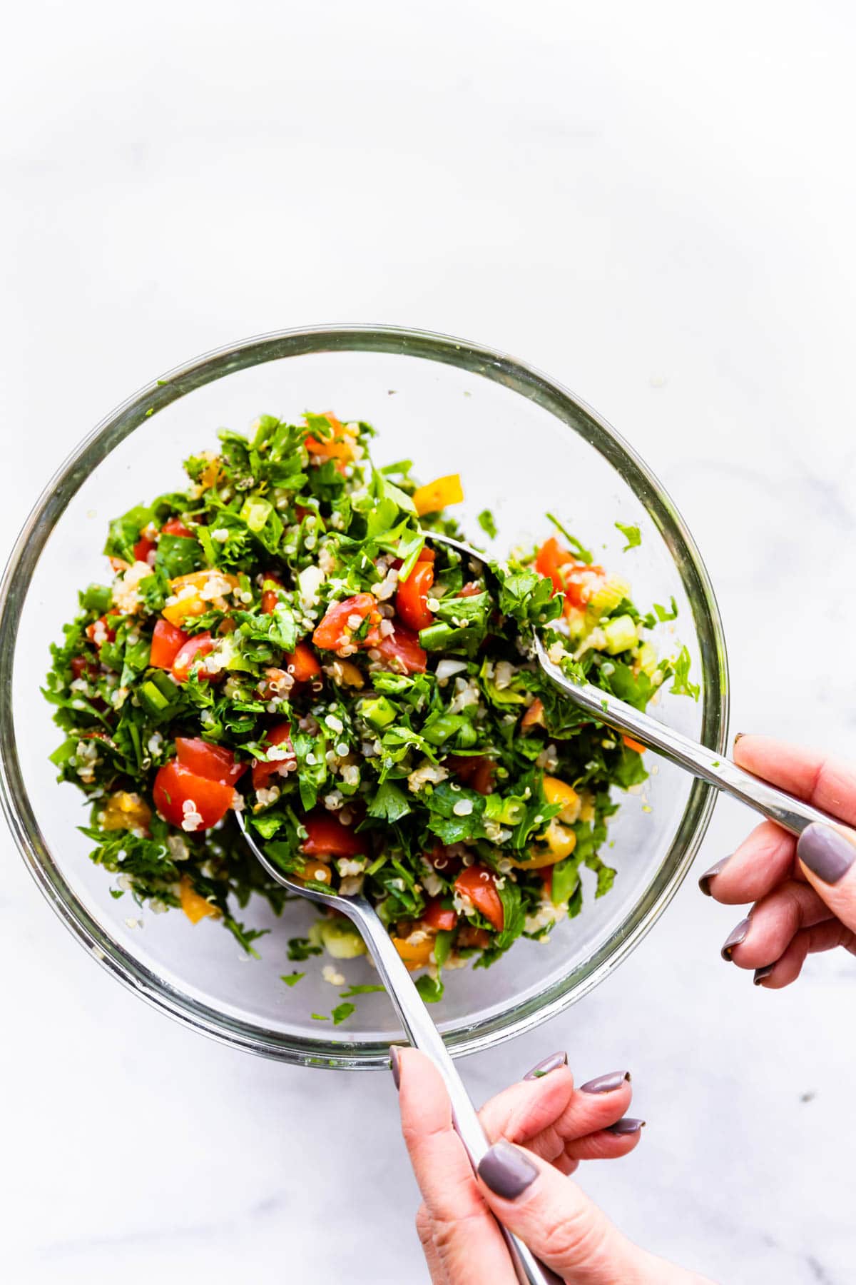 tossing gluten free tabbouleh salad ingredients in large glass bowl