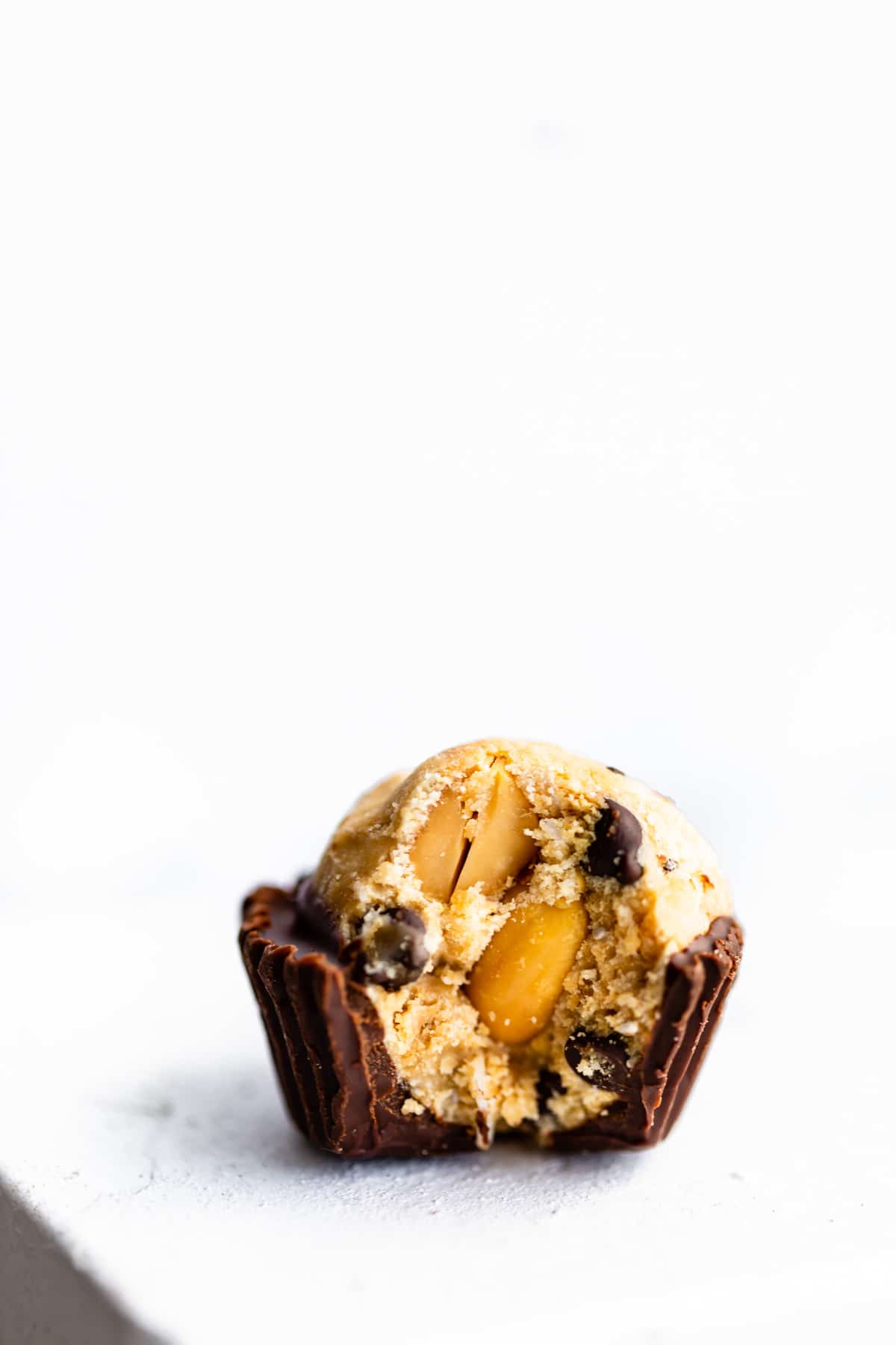 no bake cookie dough chocolate cup with bite taken from side to show inside texture with chocolate chips and nuts.