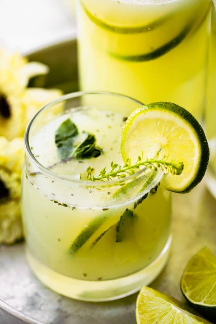 Brazilian limeade in a cocktail glass garnished with slice of lime and fresh herbs