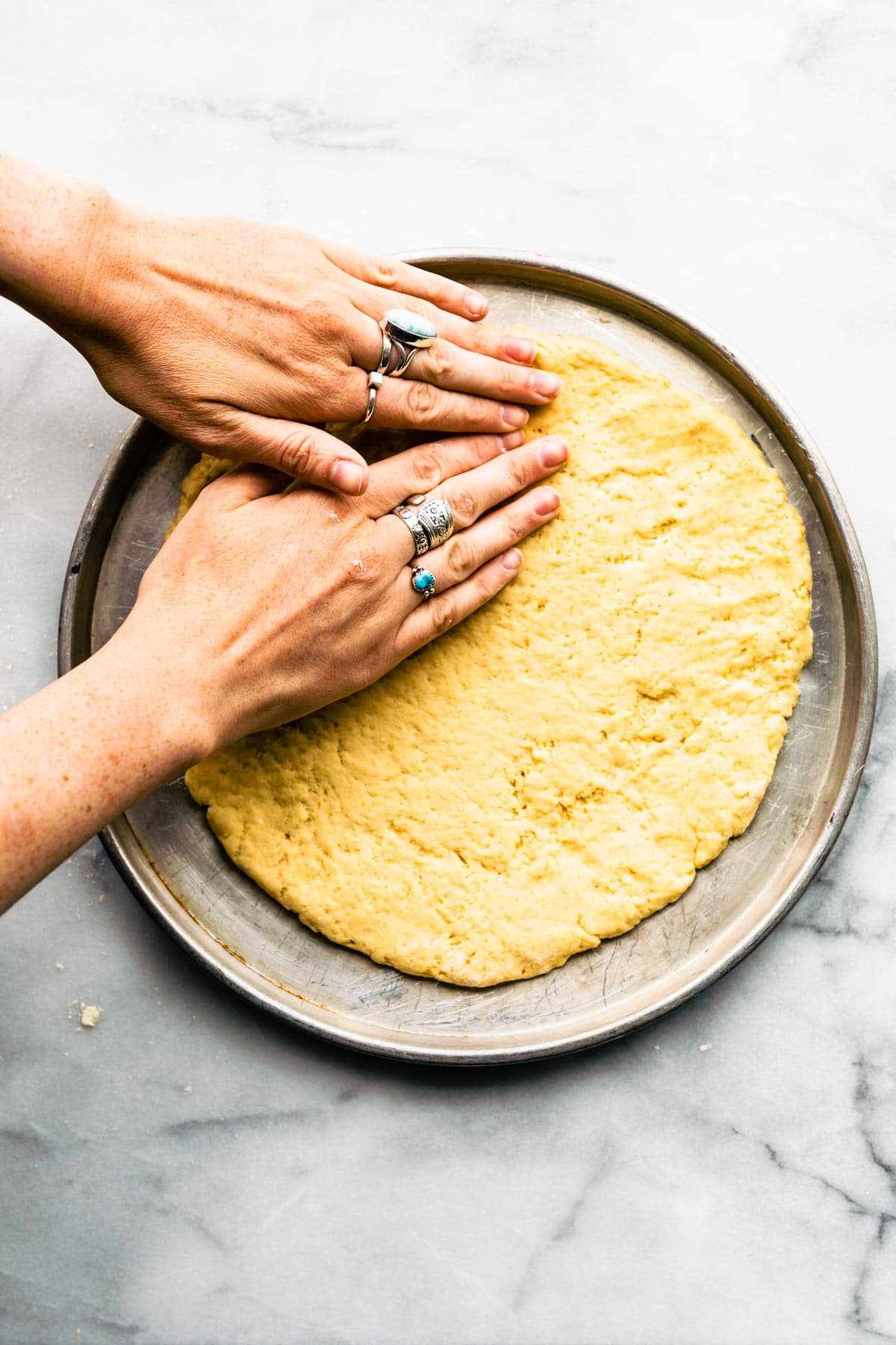 woman's hands pressing yeast free pizza dough into a pizza pan