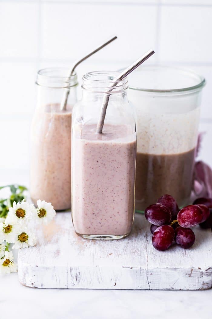 frozen grape and yogurt smoothie in 2 glasses with straws. Grapes and flowers on the sides