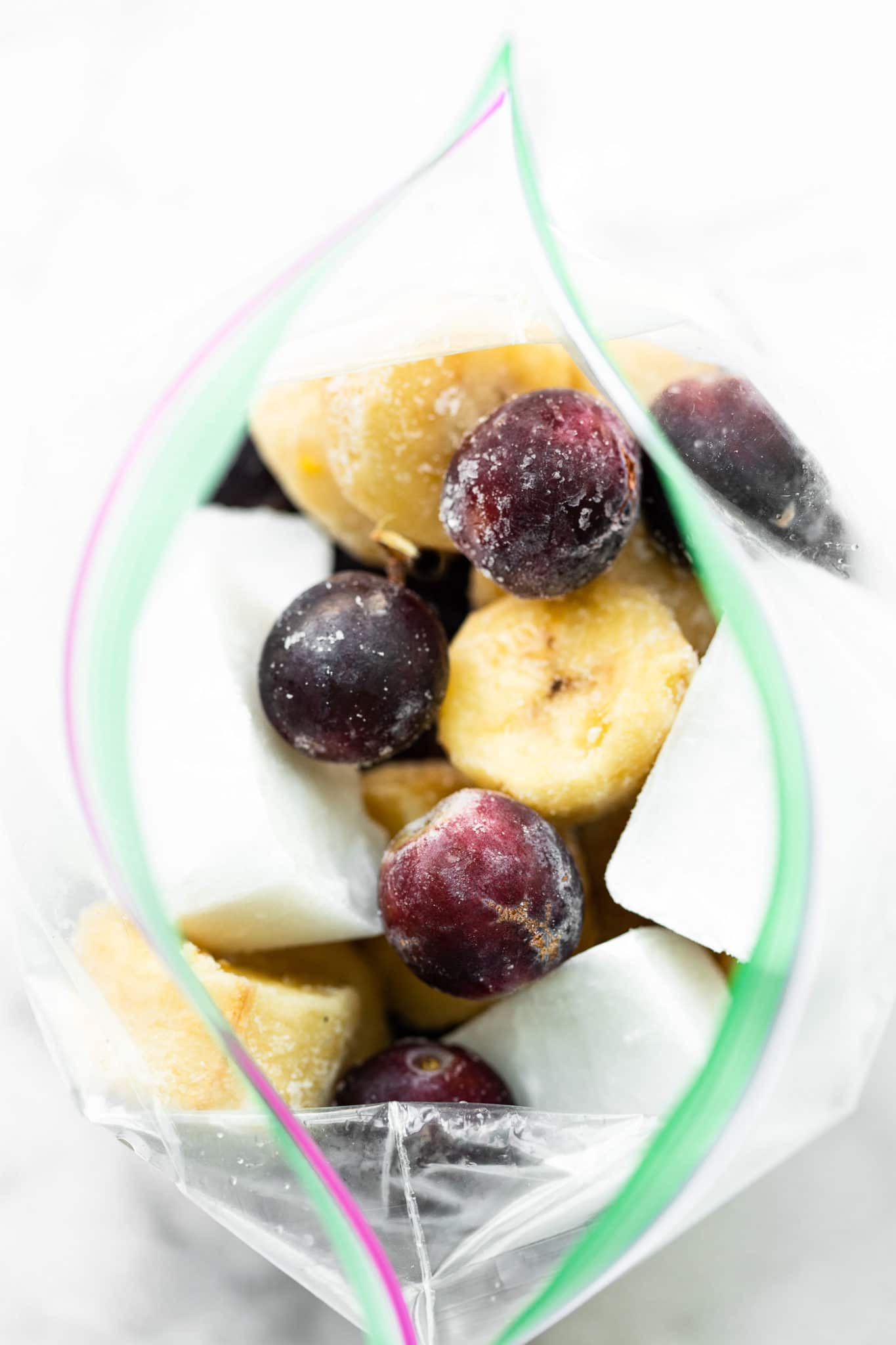 overhead image of frozen grapes, banana, and coconut milk ice cubes in a ziplock bag