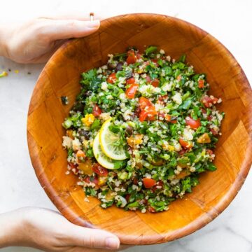woman holding wooden bowl of gluten free tabbouleh salad