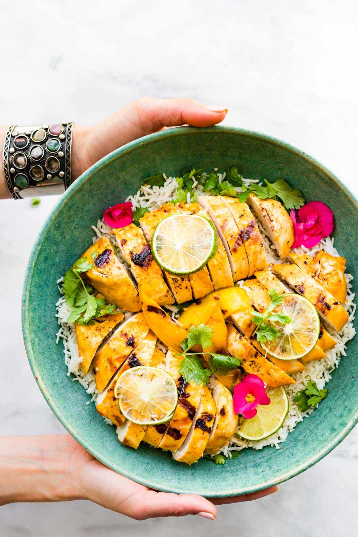 woman's hands holding green serving bowl filled with healthy mango chili chicken dinner