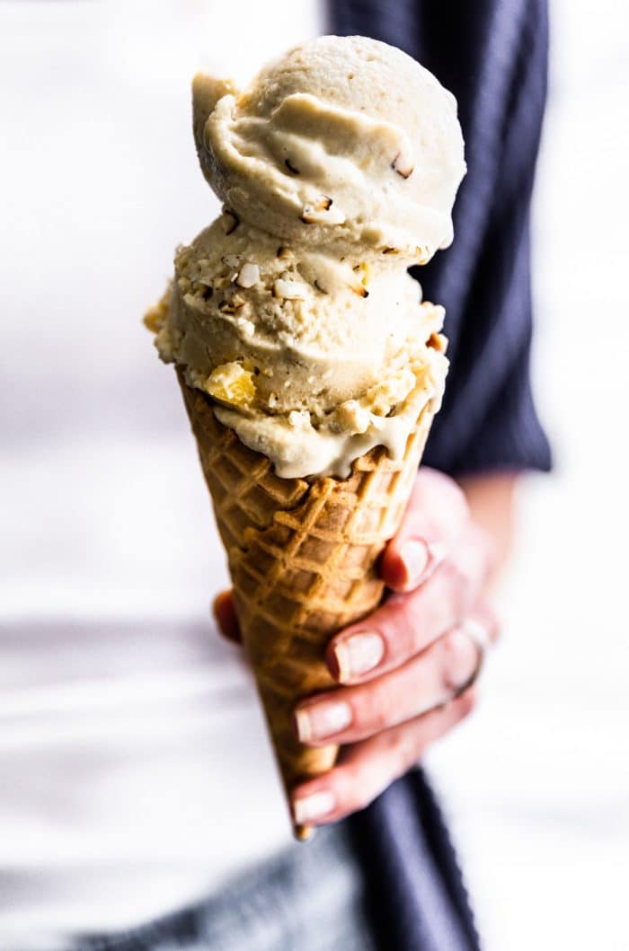 woman's hand holding dairy free dessert: double scoop of banana nice cream in waffle cone