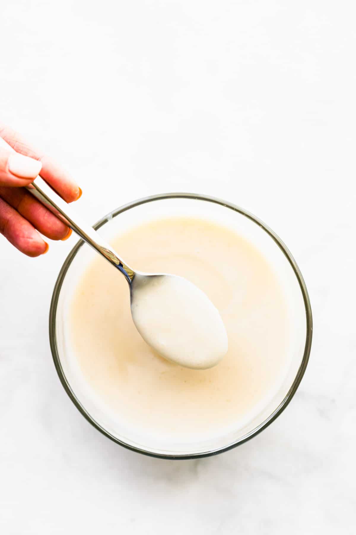 overhead shot: using spoon to remove vegan condensed milk from a bowl