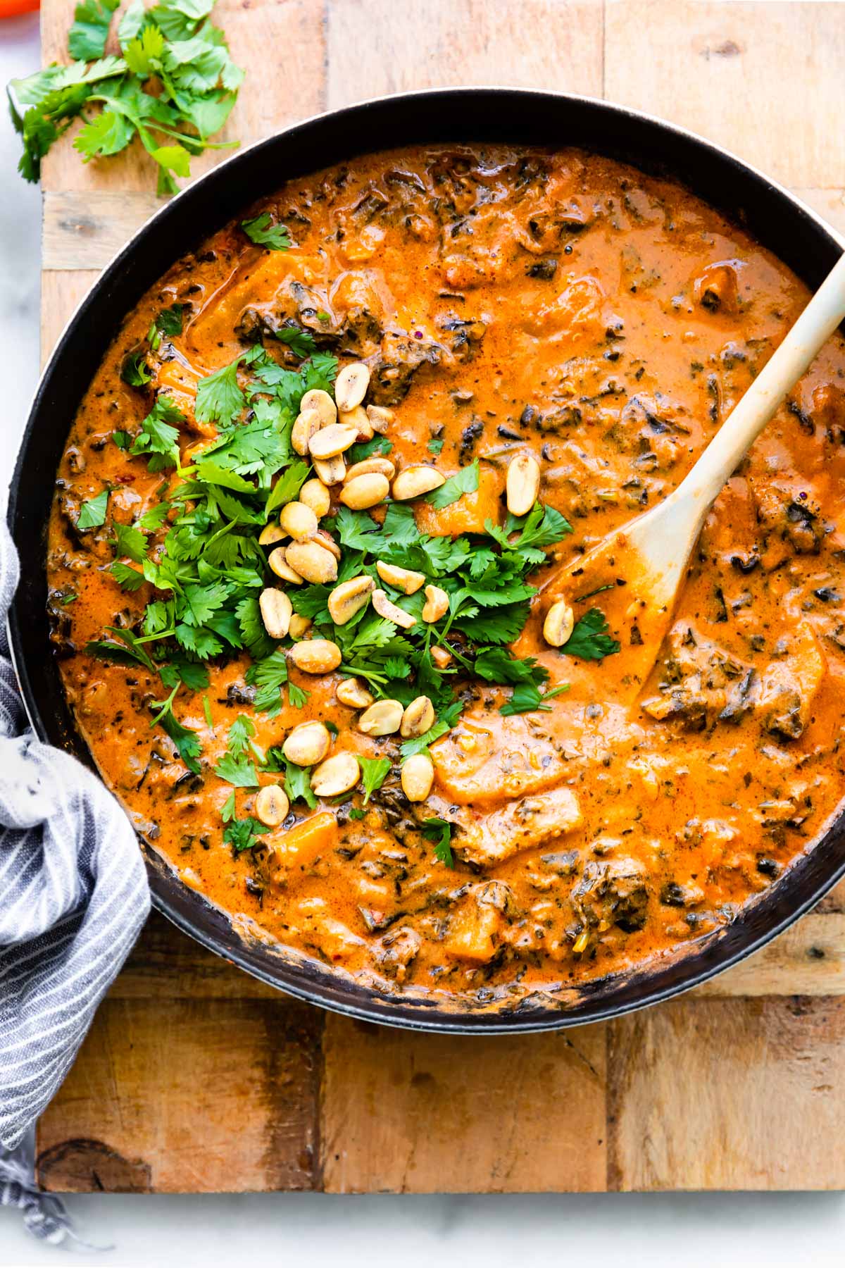 overhead photo: large pot of peanut stew; wooden spoon stirring fresh herbs in