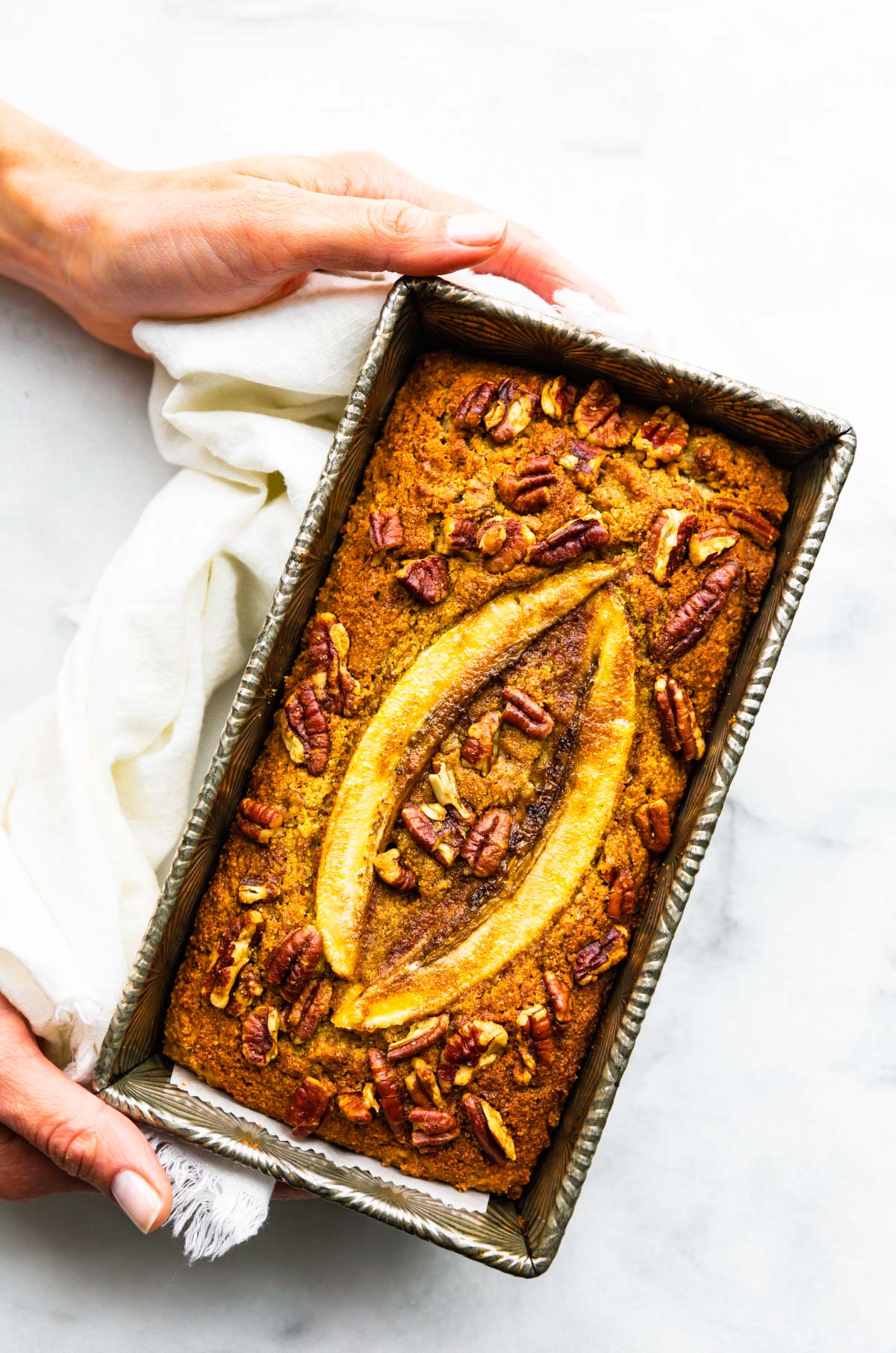 woman's hands holding loaf pan with low carb banana walnut bread