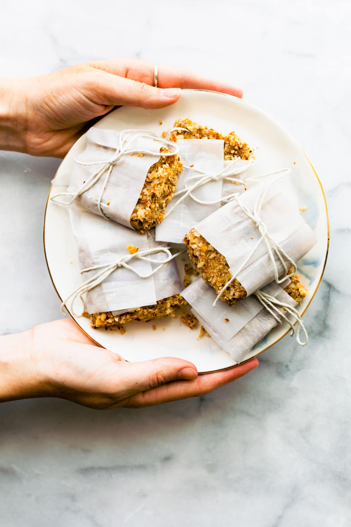 Overhead shot of paleo protein bars wrapped and tied with string on a plate being held by two hands