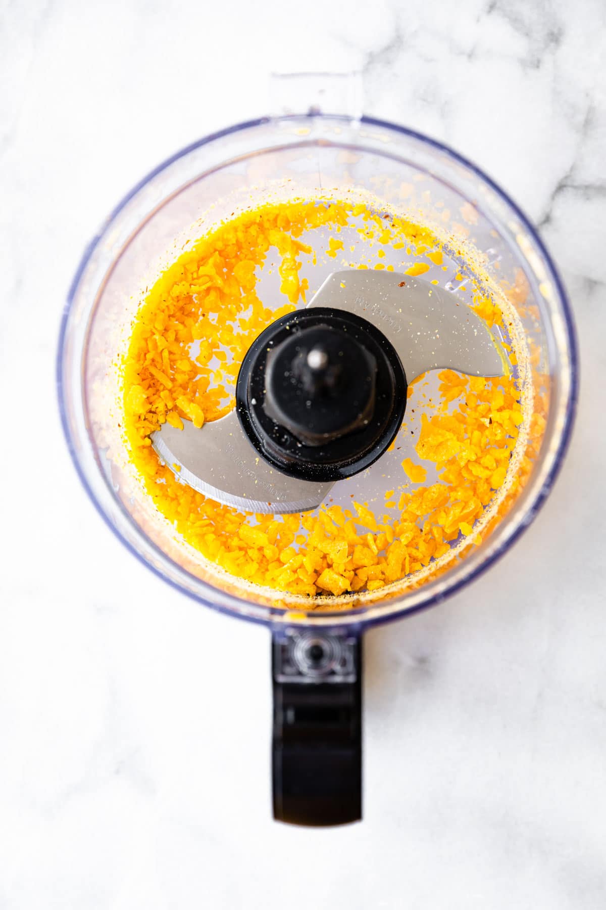 grinding dried mango in bowl of a food processor