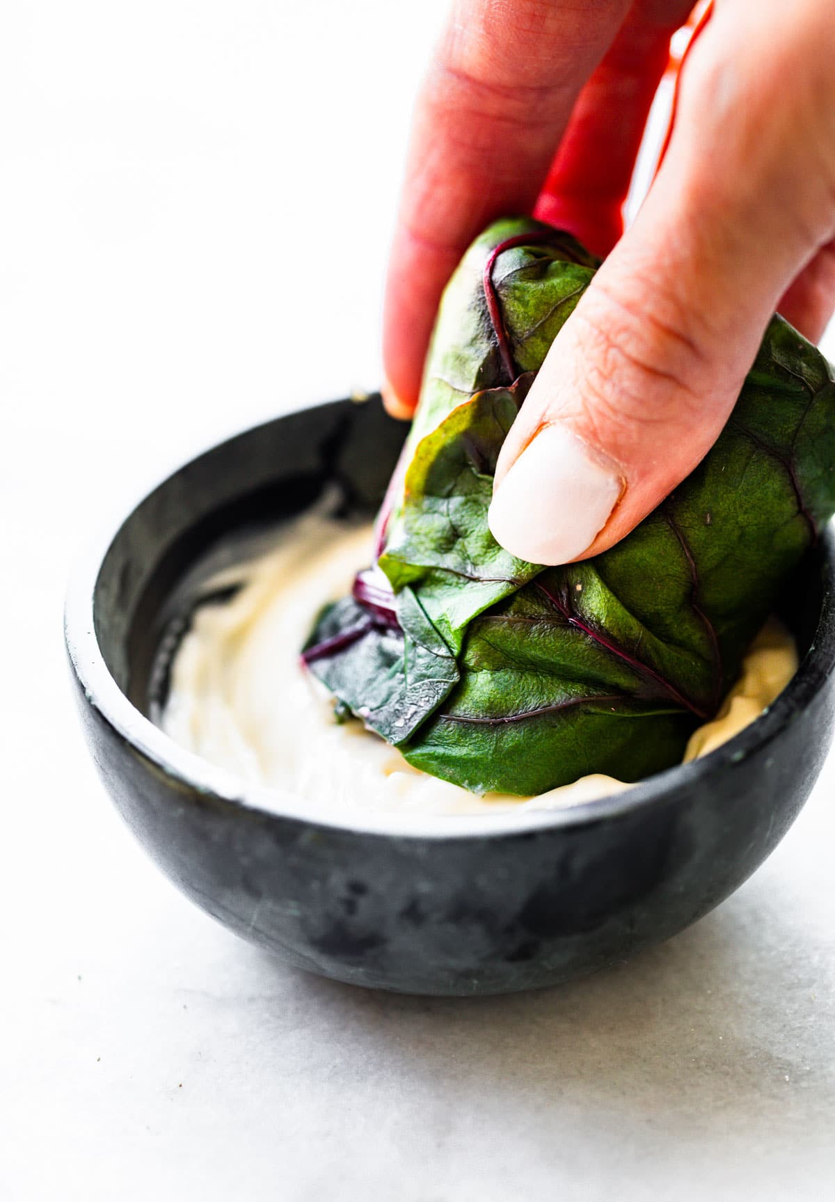 woman's hand dipping a Swiss chard salad wrap into bowl of Greek yogurt dressing