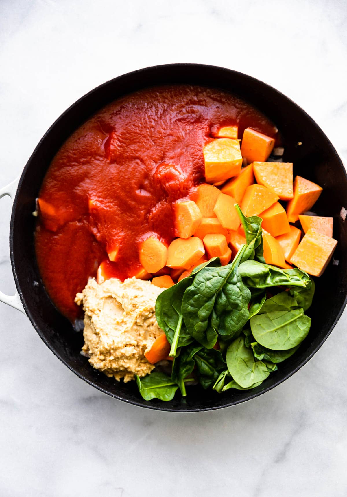 overhead photo: tomato sauce, spinach leaves and chunks of sweet potato in black pot