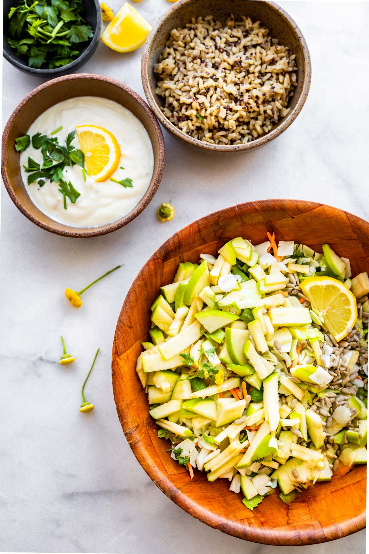 bowl of apple slaw next to smaller bowls with quinoa and white salad dressing