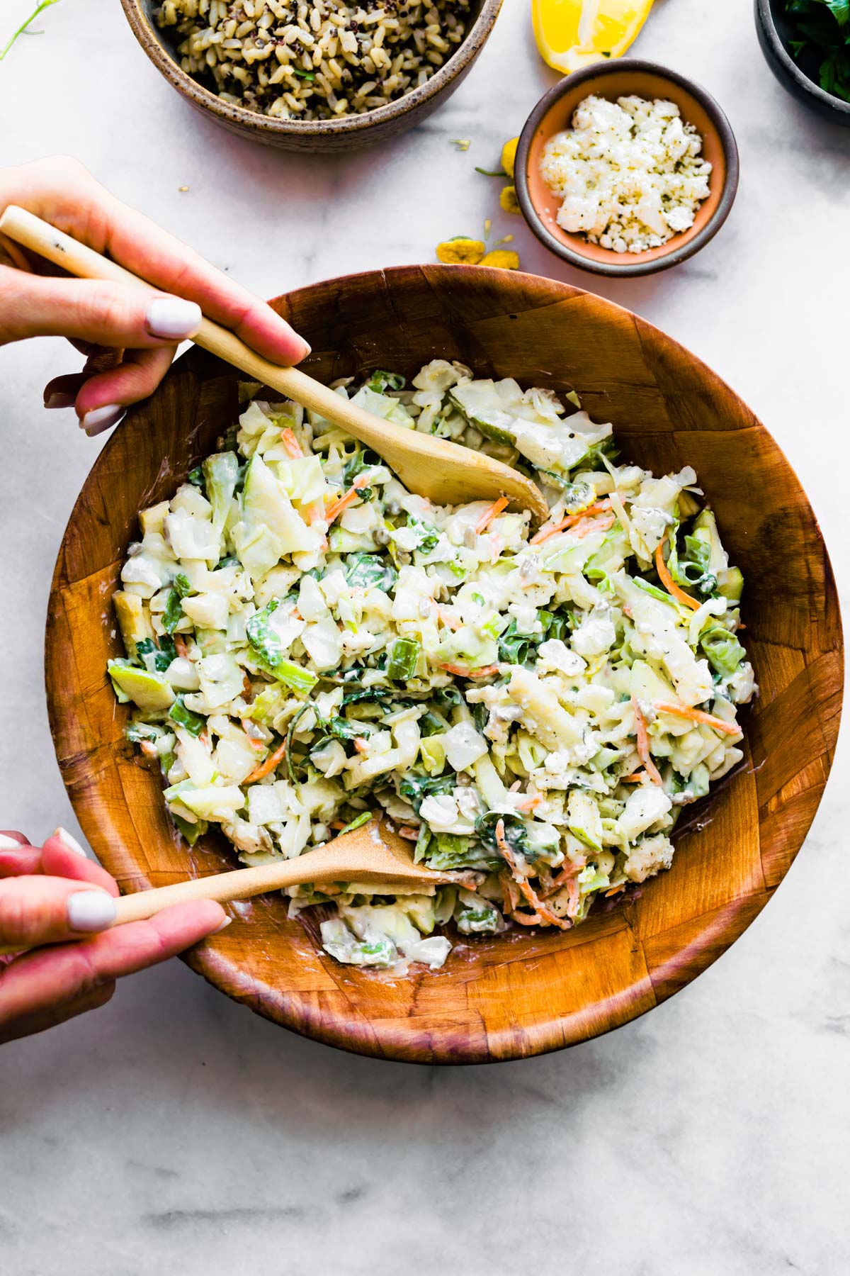 using wooden spoons to toss red cabbage apple slaw in wooden bowl