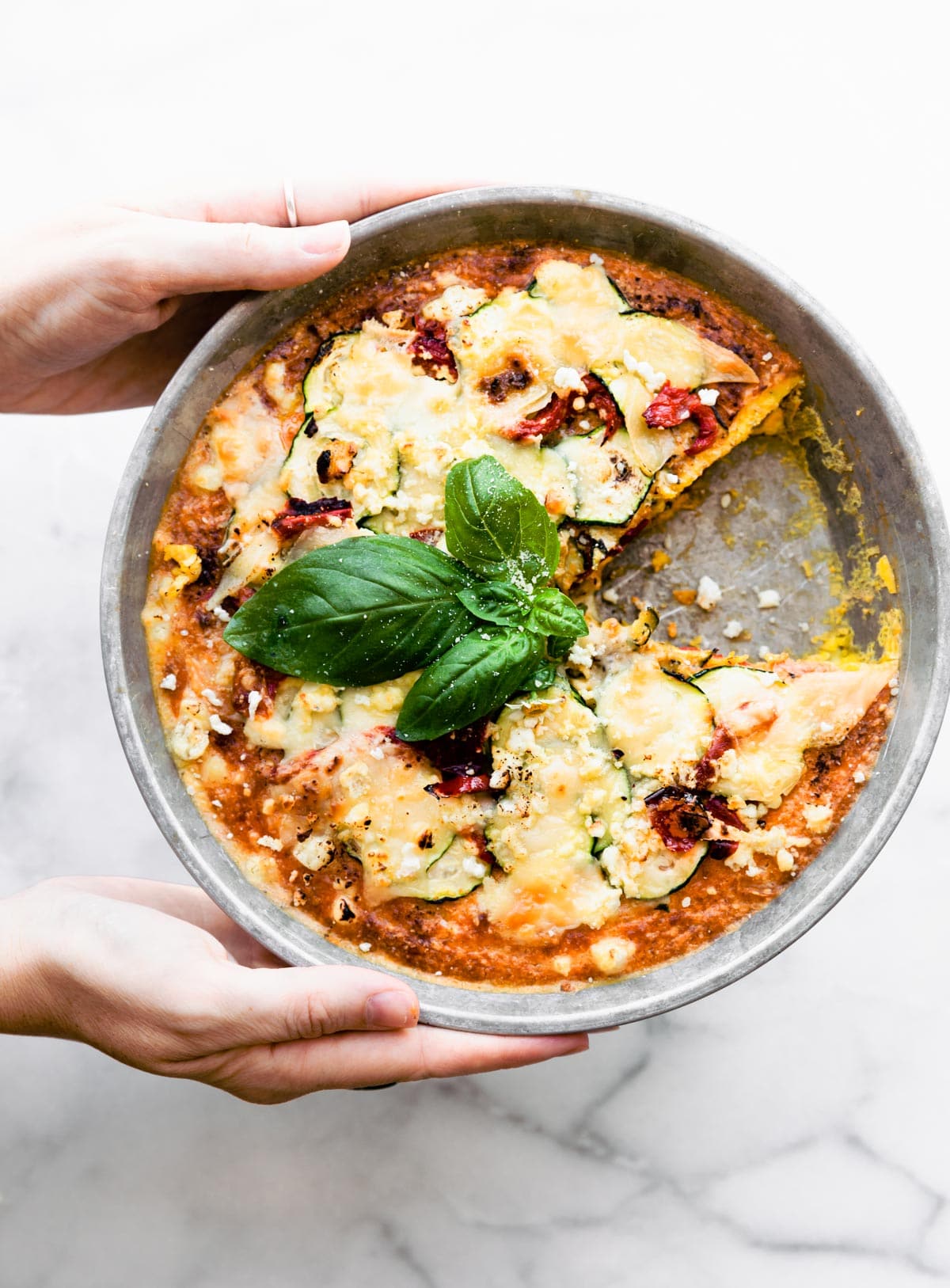 overhead photo: woman's hands holding a crustless keto quiche with one slice removed