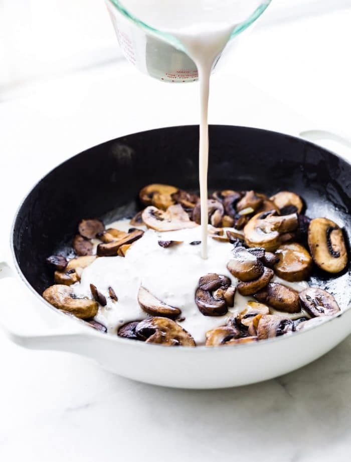 adding coconut cream to sliced mushrooms in a white skillet