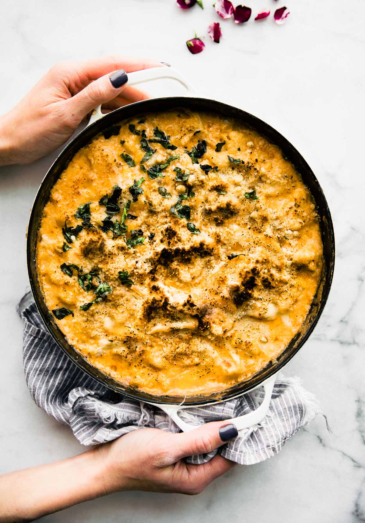 Two hands holding skillet filled with baked mac and cheese