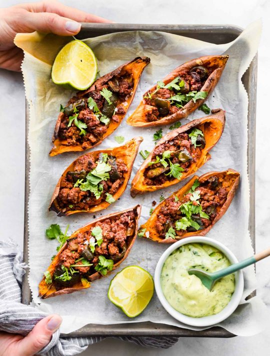 overhead photo: hands holding parchment paper lined tray of sweet potato skins filled with chili