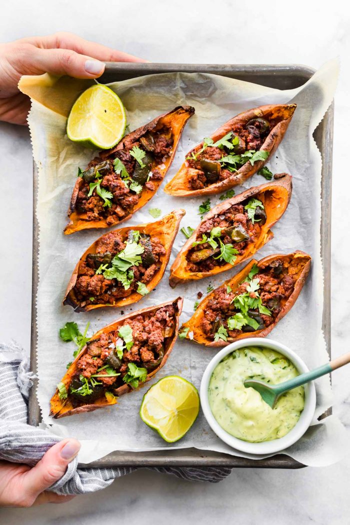 overhead photo: hands holding parchment paper lined tray of sweet potato skins filled with chili
