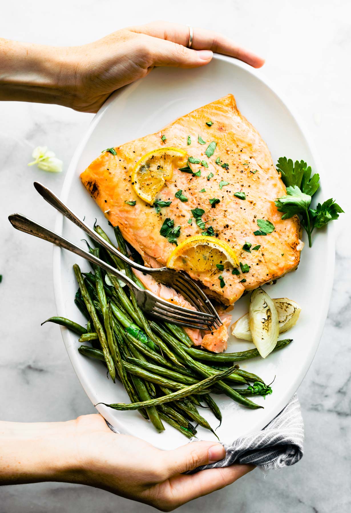 overhead: woman's hands holding plate of maple mustard salmon with French green beans