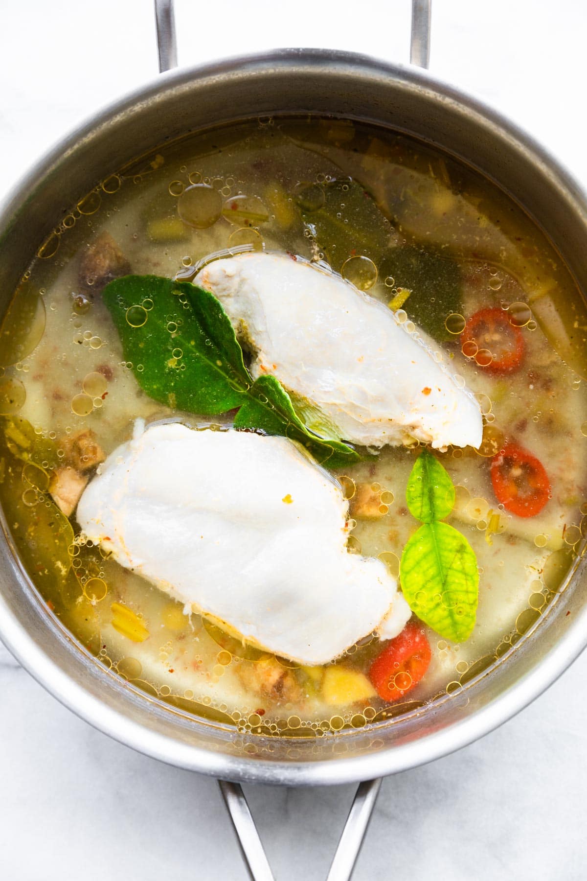 Overhead photo of Thai Chicken Soup in a large pot with poached chicken and herbs.