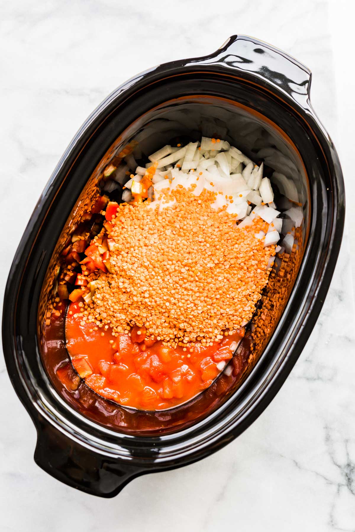 overhead image lentils, diced onion, and tomatoes in a crockpot