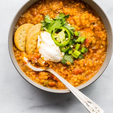 overhead photo: spoon in bowl of slow cooker chili garnished with crackers, jalapeno slices and sour cream