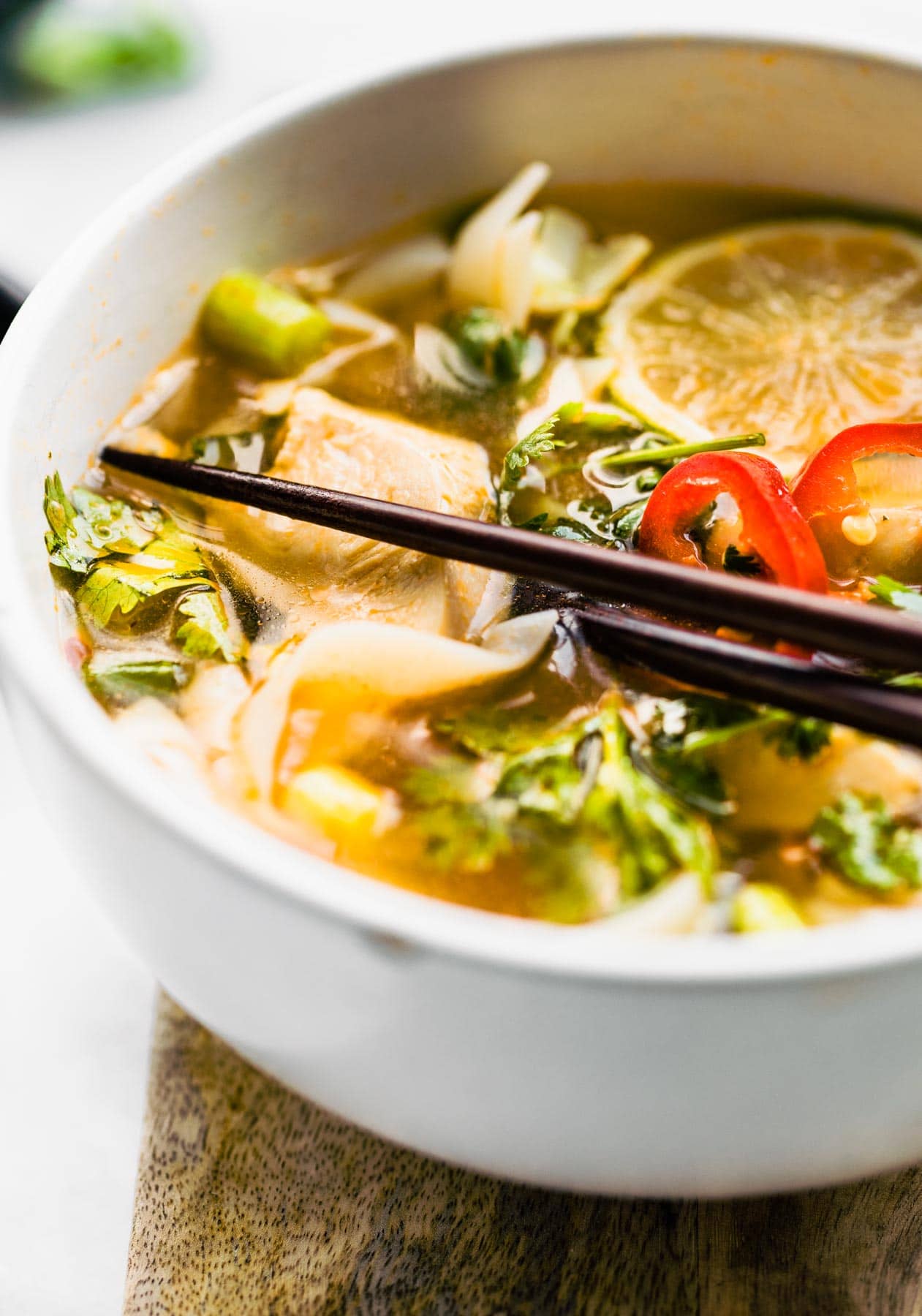thai soup with chicken in white bowl with wooden chopsticks