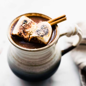 Mexican hot chocolate cocktail in a mug garnished with cinnamon stick and toasted marshmallows.
