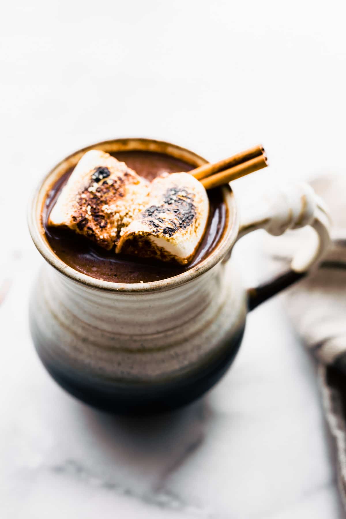 Mexican hot chocolate cocktail in a mug garnished with cinnamon stick and toasted marshmallows