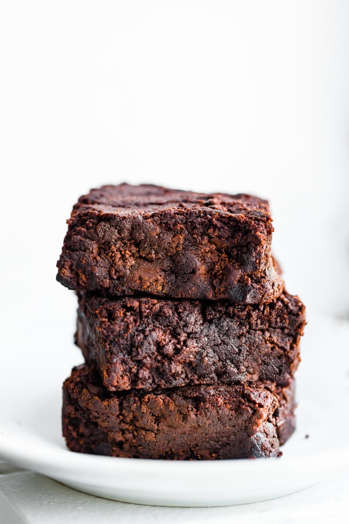 Three dark chocolate gluten-free brownies stacked up on a white plate.