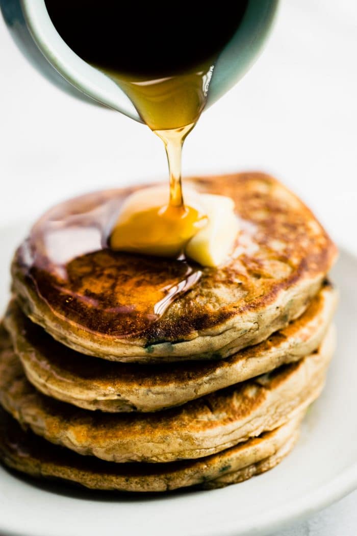 pouring syrup from pitcher onto tall stack of pancakes