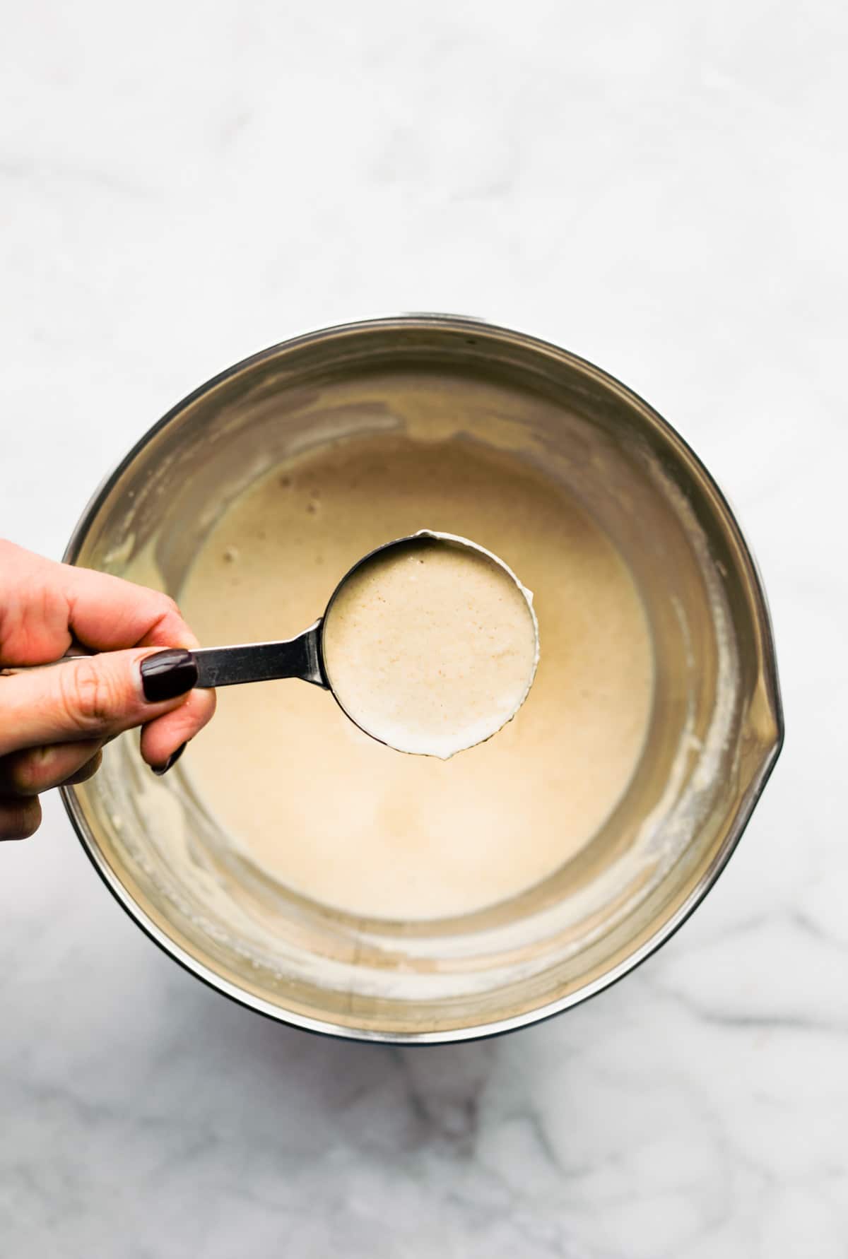 using metal measuring cup to scoop pancake batter from a bowl