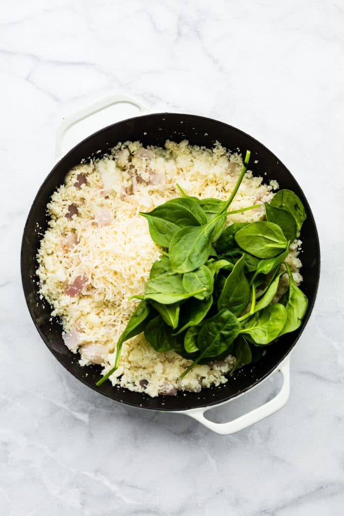 raw baby spinach on top of cauliflower rice in pan
