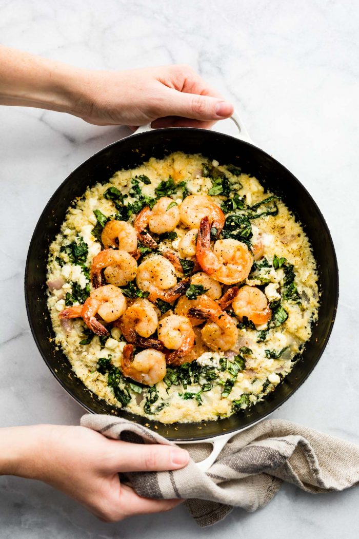 Two hands holding skillet filled with cauliflower risotto shrimp skillet.