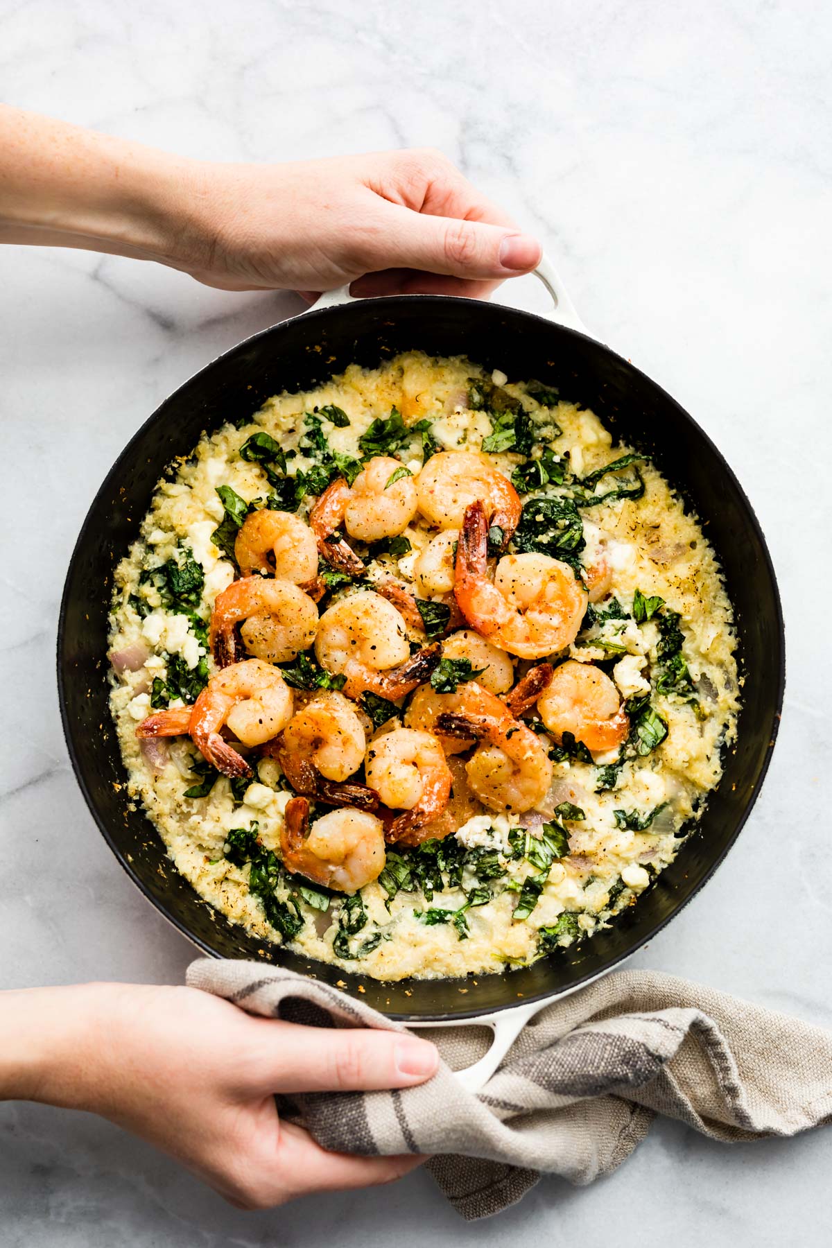 woman's hands holding pan of cauliflower risotto shrimp skillet