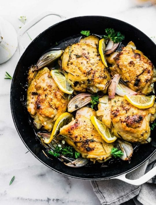 bone-in chicken thighs with crispy skin in skillet with lemon slices and onions