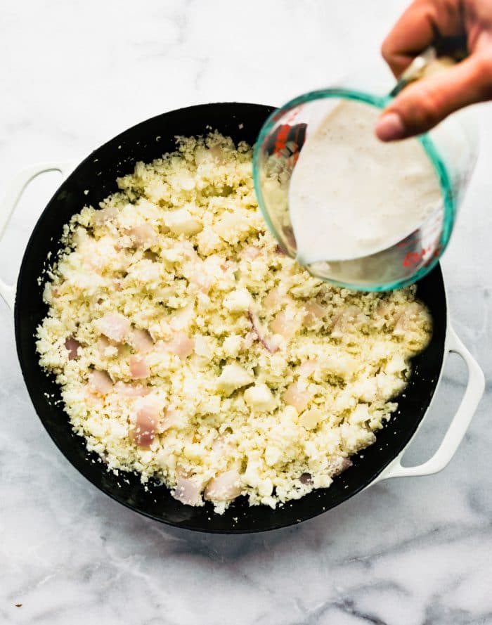 adding dairy free cream to pan of cooked cauliflower rice to make risotto
