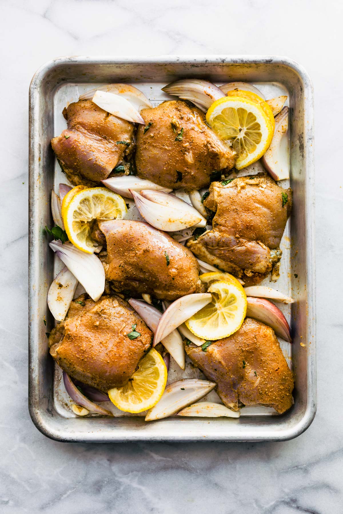 baked chicken thighs on sheet pan with slices of lemon and onions