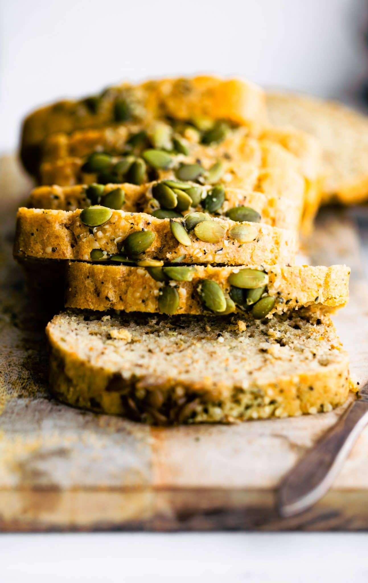 a close up of sliced nut bread with poppy seeds and pumpkin seeds on top sitting on a wooden cutting board