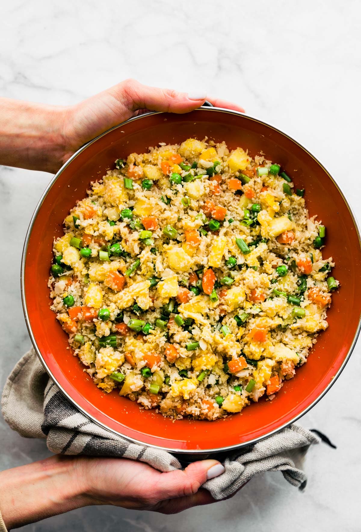Two hands holding a bowl filled with paleo cauliflower pineapple fried rice.