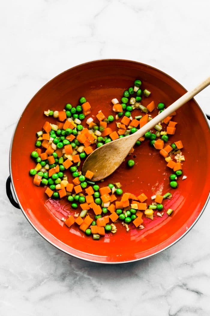 peas and diced carrots cooking in red skillet