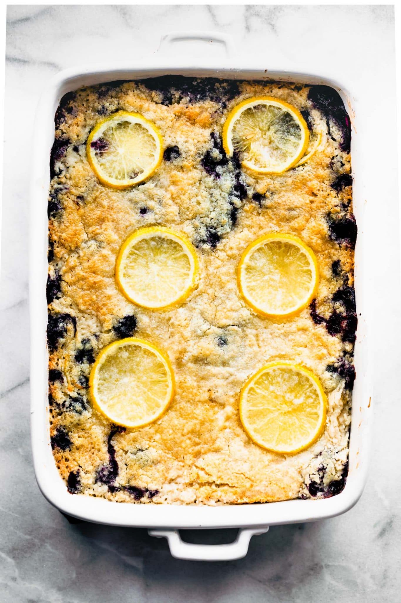 Overhead view lemon blueberry cake topped with baked-in lemon slices in white baking dish.