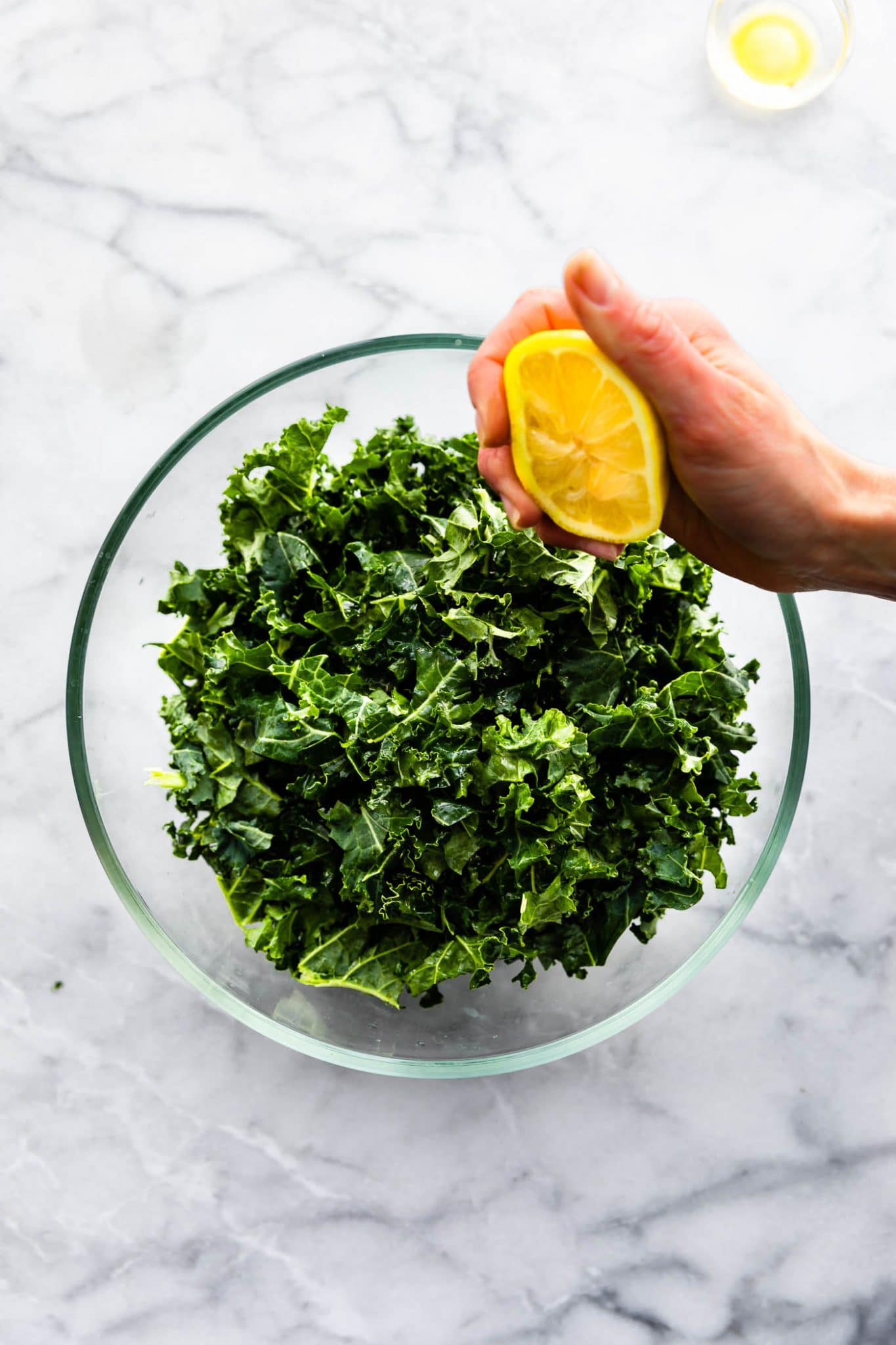 A hand squeezing fresh lemon over chopped fresh kale in clear glass bowl.