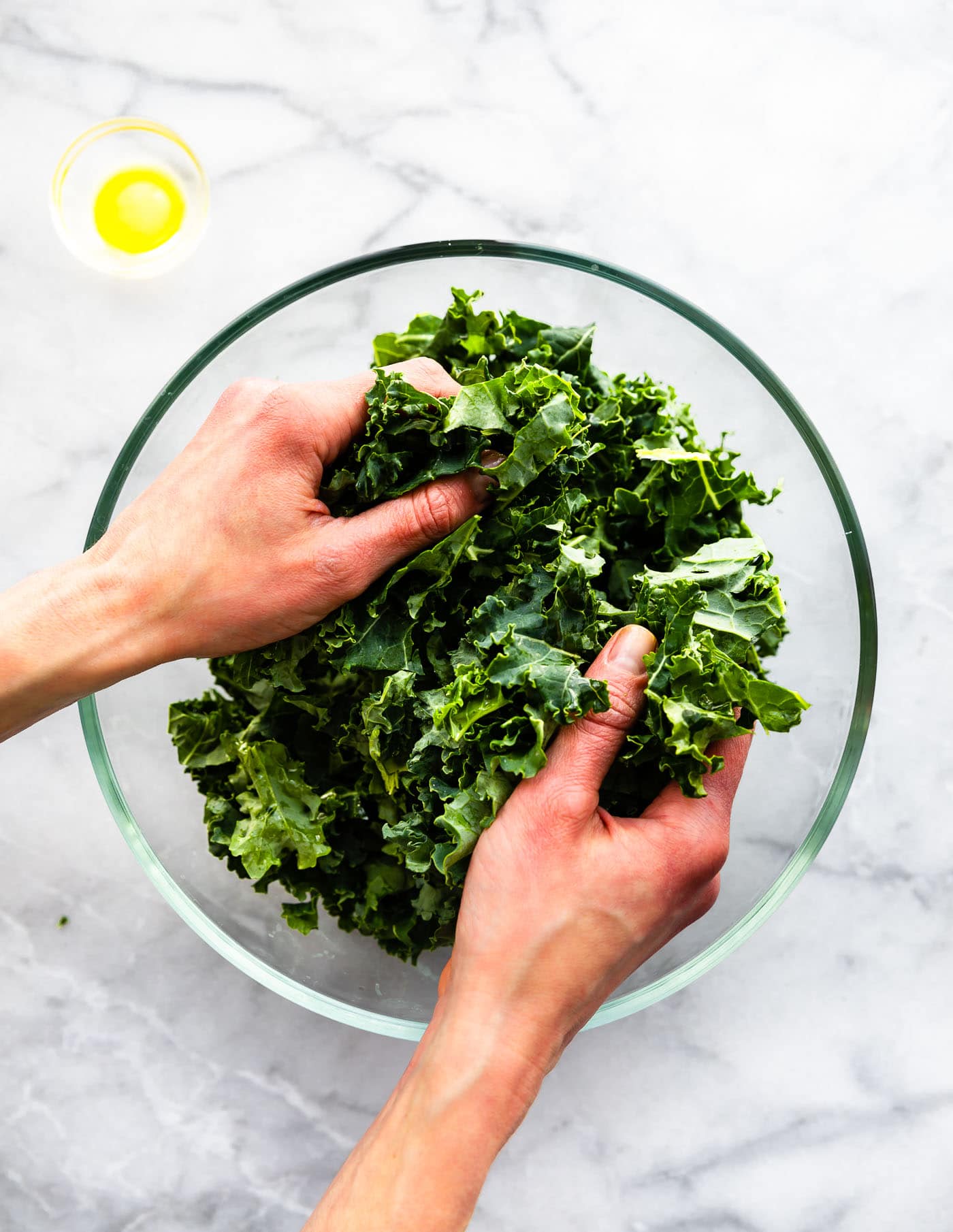 overhead photo of womans' hands massaging kale in glass bowl