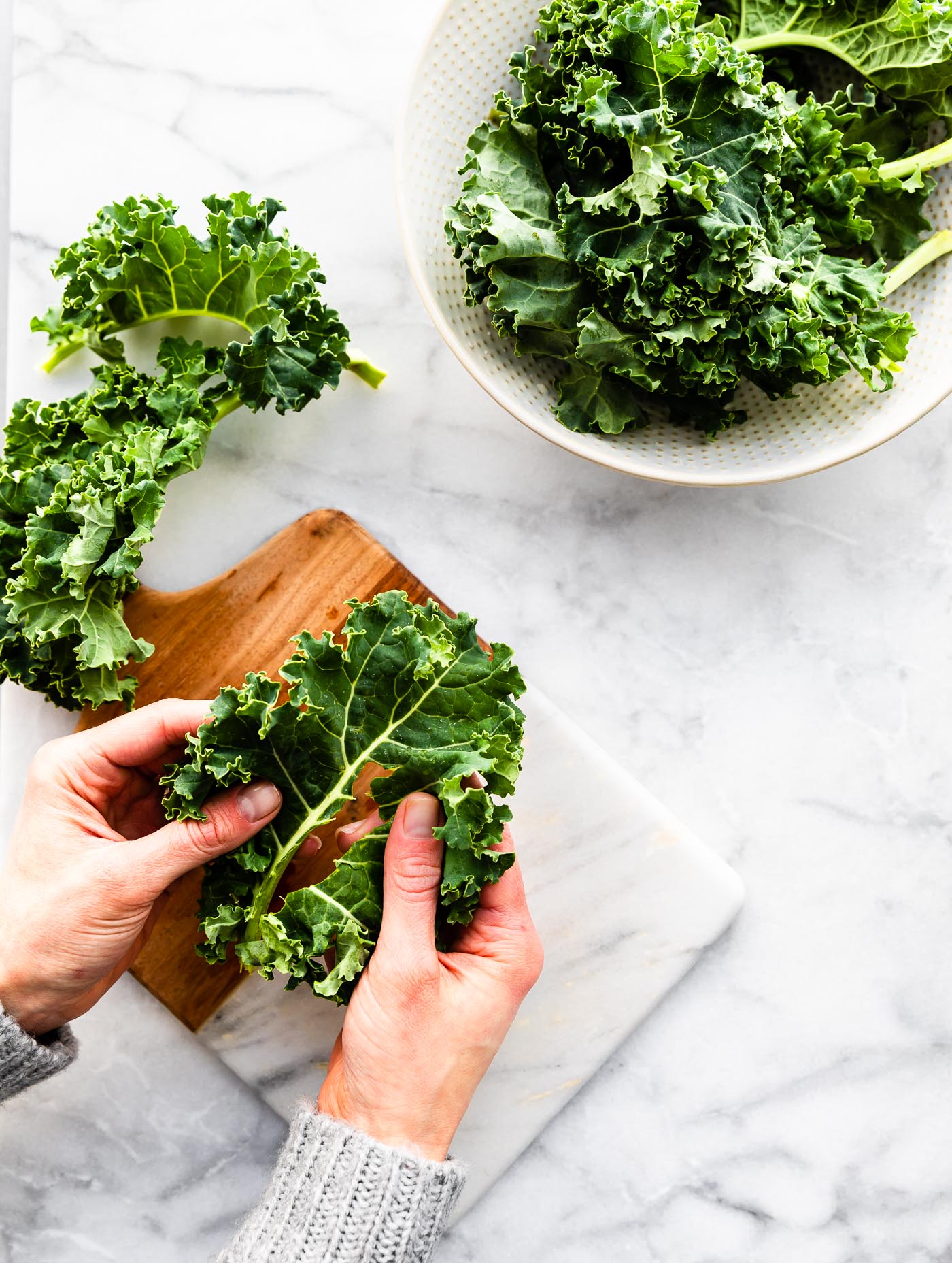 Two hands ripping kale leaf from stalk over a cutting board.