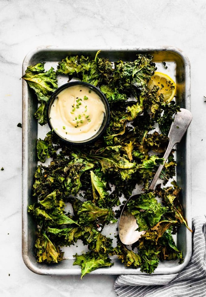Overhead image of prepared crispy kale chips with vegan ranch dipping sauce cup on a cookie sheet