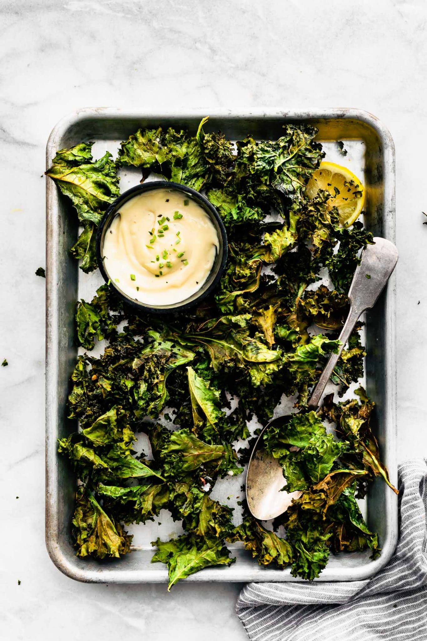 Overhead image of prepared crispy kale chips with vegan ranch dipping sauce cup on a cookie sheet
